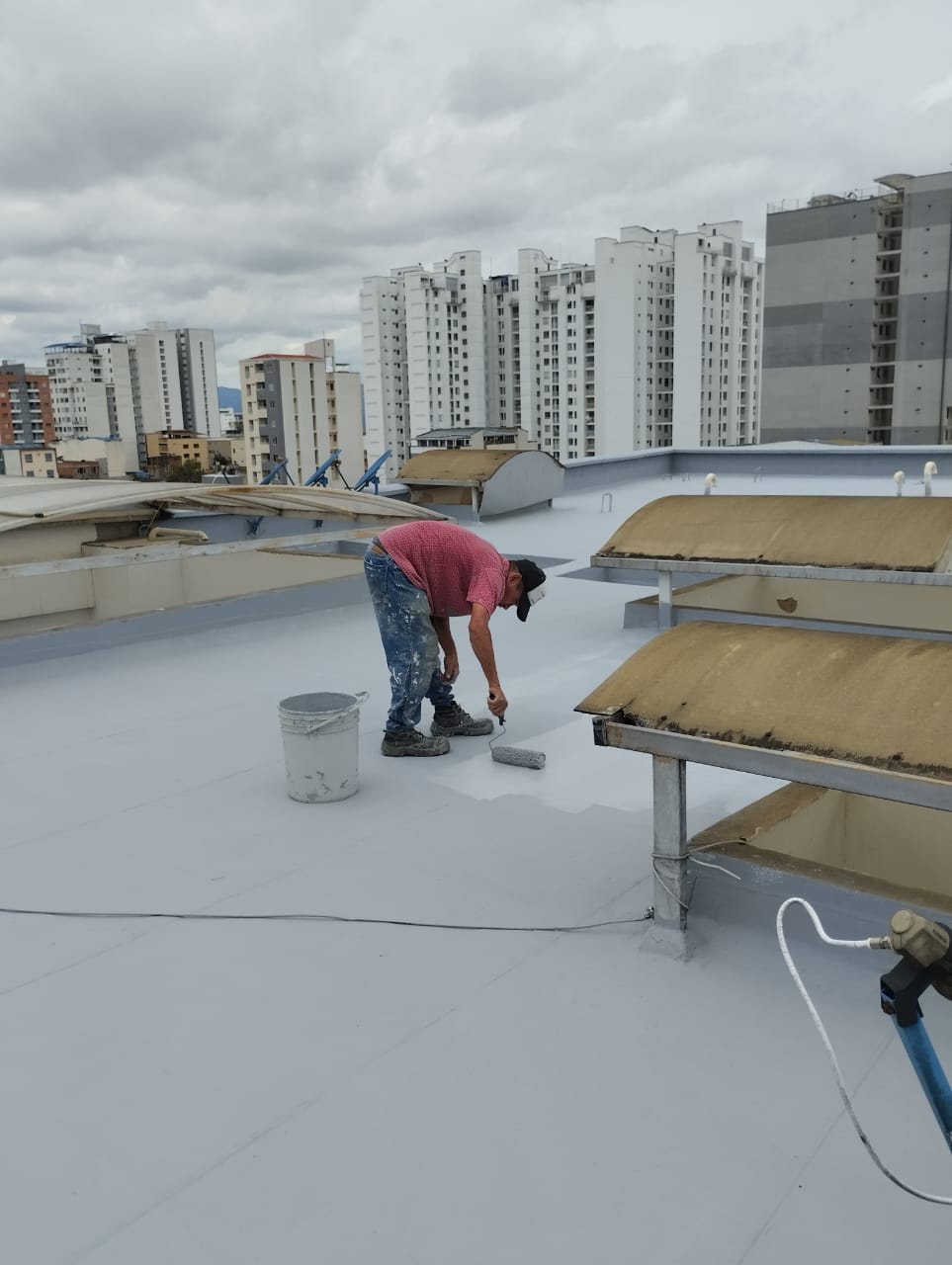 Técnico aplicando pintura o membrana impermeabilizante sobre una placa de techo.